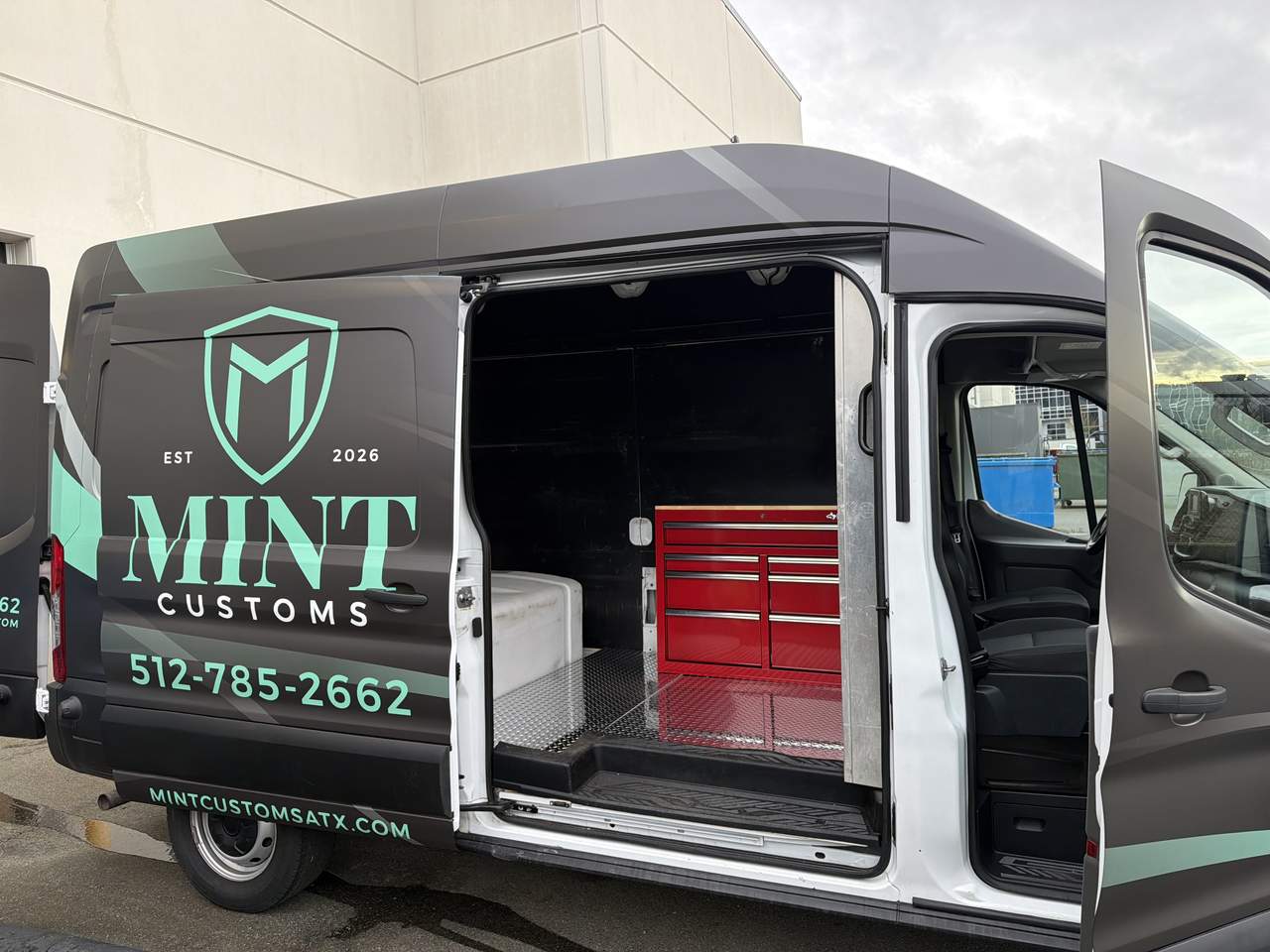 Close-up of a MINT Customs branded mobile detailing van with the rear cargo door open, showing onboard equipment used for mobile car detailing